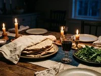 Mesa com pão sem fermento, taça de vinho, ervas e velas acesas sobre toalha de linho