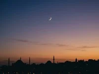 Lua crescente fina no céu do entardecer sobre silhuetas de cúpulas e minaretes Lua crescente fina no céu do entardecer sobre silhuetas de cúpulas e minaretes