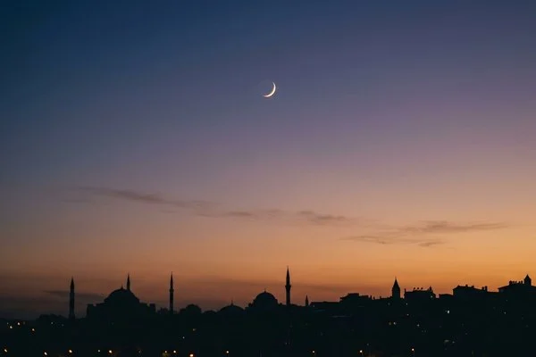 Lua crescente fina no céu do entardecer sobre silhuetas de cúpulas e minaretes Lua crescente fina no céu do entardecer sobre silhuetas de cúpulas e minaretes
