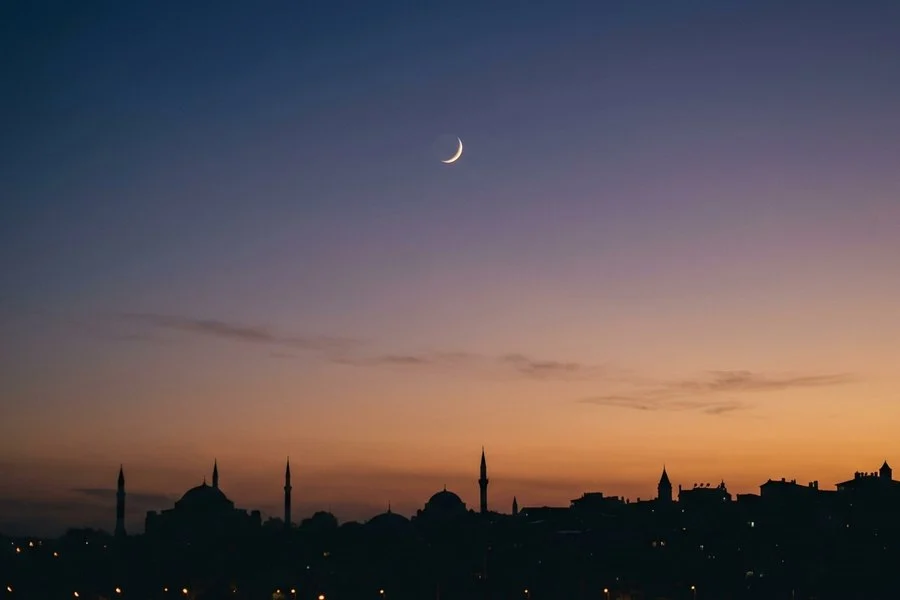 Lua crescente fina no céu do entardecer sobre silhuetas de cúpulas e minaretes Lua crescente fina no céu do entardecer sobre silhuetas de cúpulas e minaretes